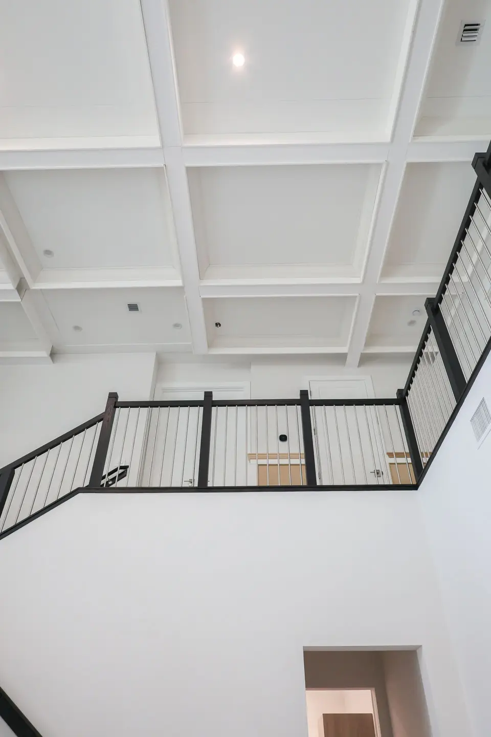 Coffered ceiling above a second-floor loft with a modern metal railing